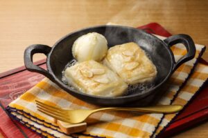 Butter-fried mochi topped with sliced almonds and cream cheese in a small skillet