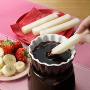 Toasted mochi sticks being dipped in melted chocolate, with strawberries and banana